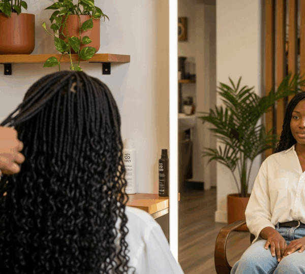 Femme noire aux cheveux crépus lissés, recevant des soins capillaires dans un salon, lumière naturelle, ambiance professionnelle.